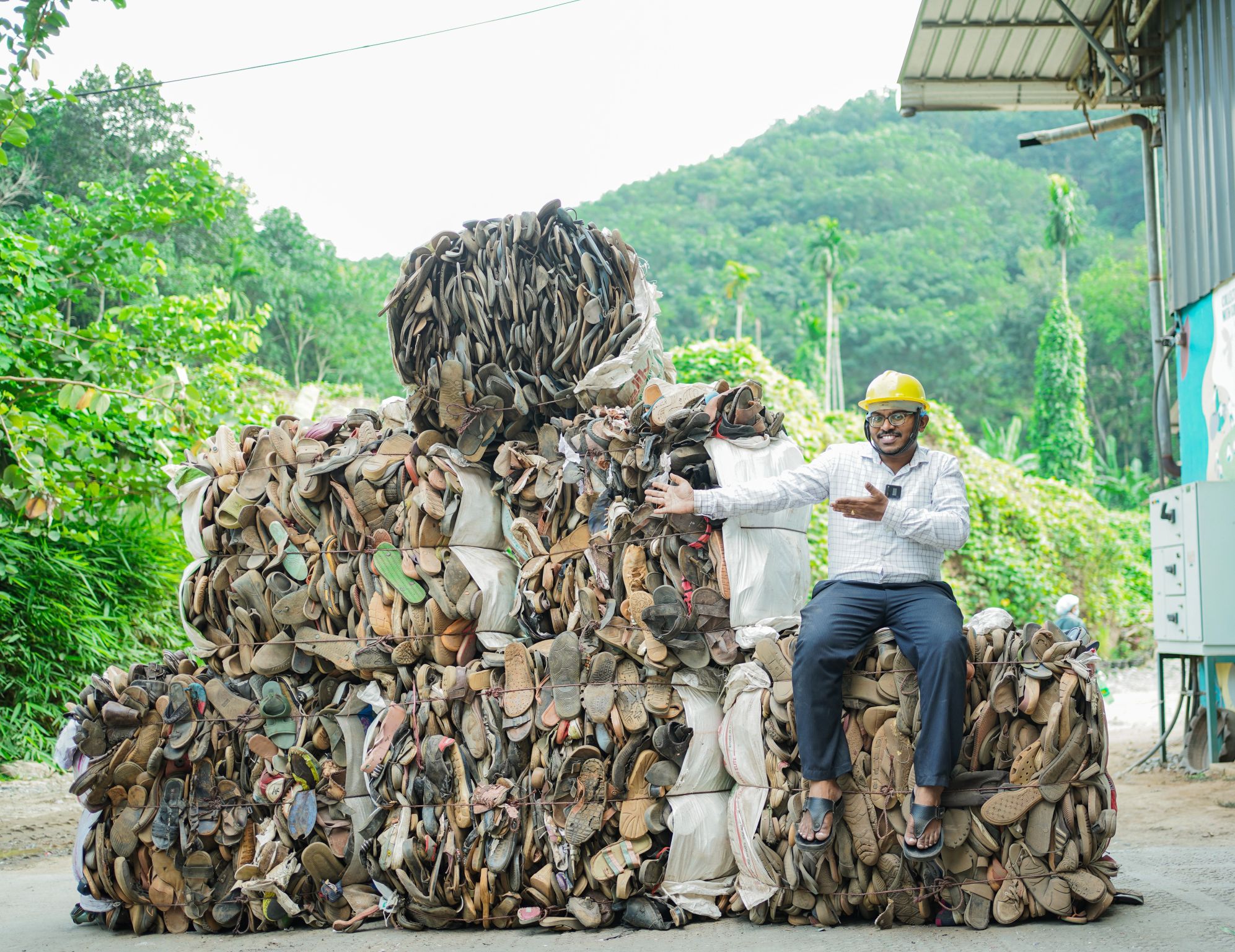 Worker on massive pile of collected shoes showing scale of footwear recovery operations